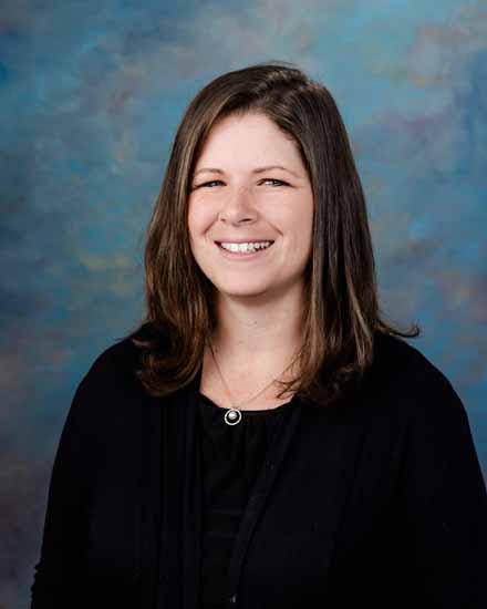 Portrait of Angela Barnhart smiling with a blue background.