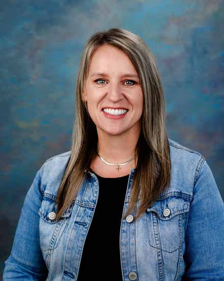 Beth Ware, a smiling woman with blonde hair, wearing a denim jacket and a cross necklace.