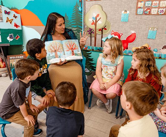 A teacher reads a colorful picture book to a young class of students