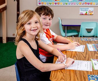 Two students smile for a photo as they complete their assignments