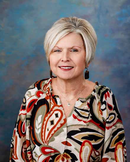 Jennifer Chambers portrait with short blonde hair and a colorful patterned blouse.