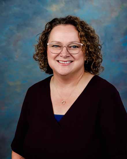 Kaylene Bailey portrait; smiling woman with curly hair and glasses.