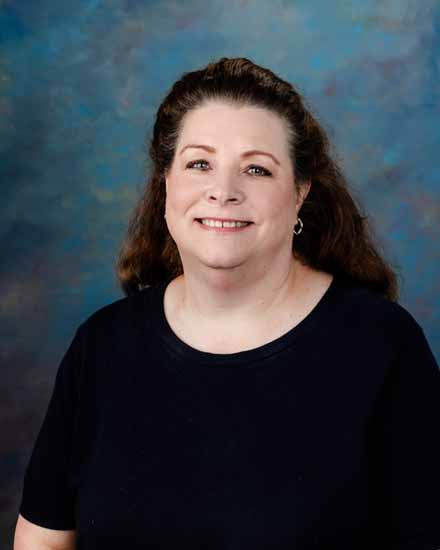 Portrait of Kim Rock, smiling with shoulder-length brown hair and a black shirt.