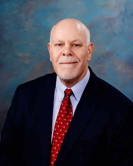 Paul Foltz portrait; man in suit and tie against a blue background.