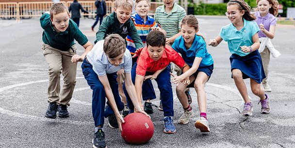 Young students run to grab a red rubber ball during recess