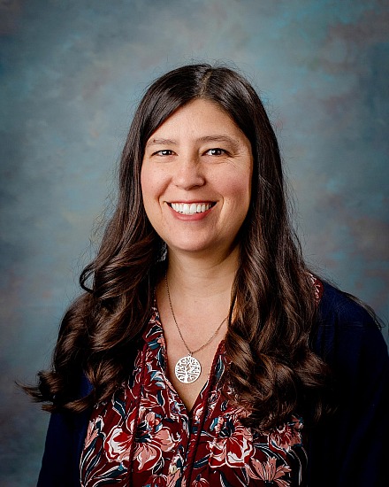 Stacia Harmon smiles in a portrait, wearing a floral top and a tree of life pendant.